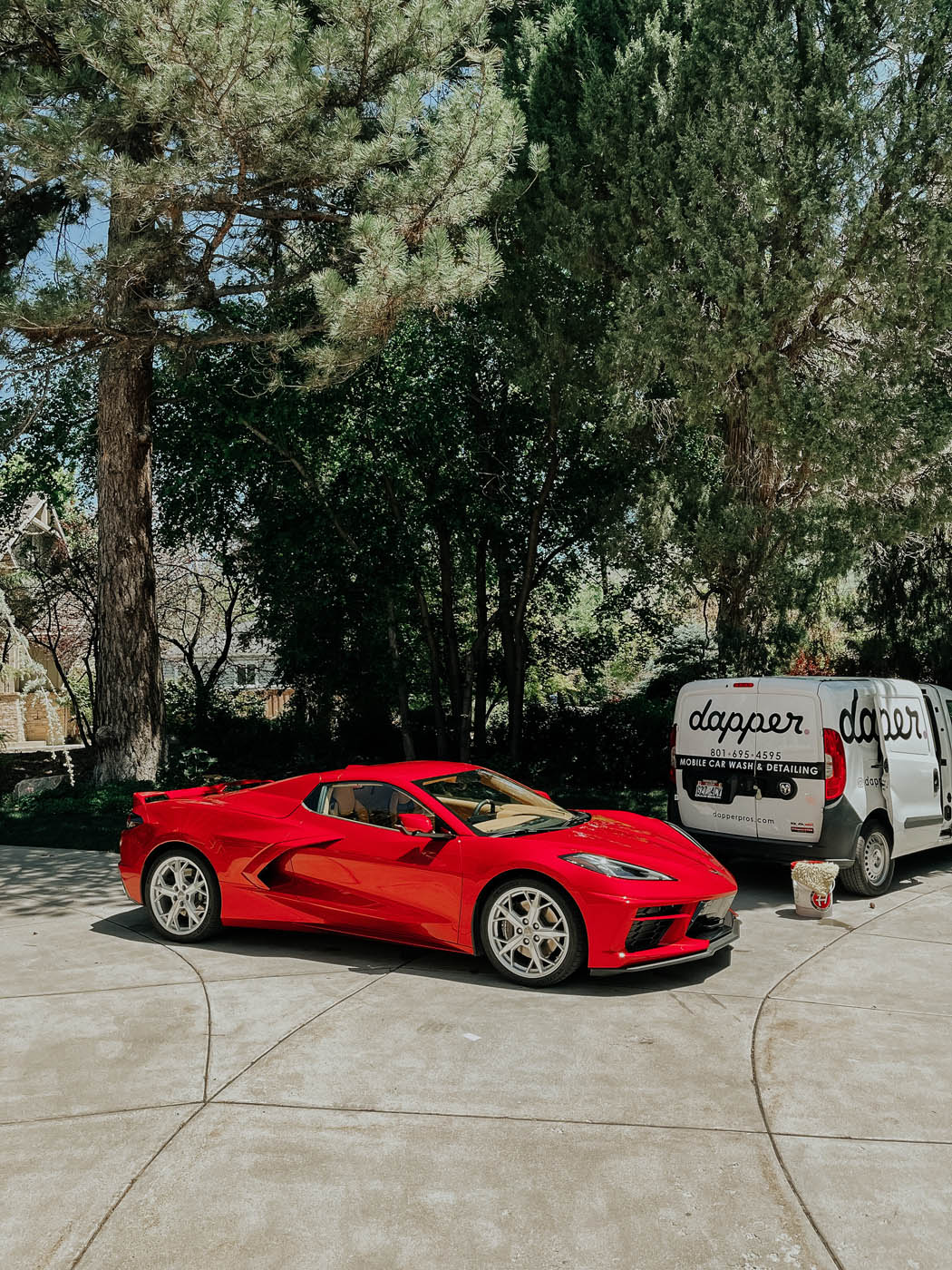 A red corvette parked next to a Dapper Pros cleaning van.